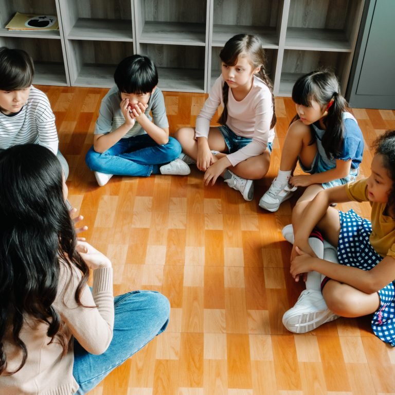 Elementary international students group sit cross legged in circle around the teacher and listening a story. Discussion group of children and teacher in classroom at school.Education, learning Concept